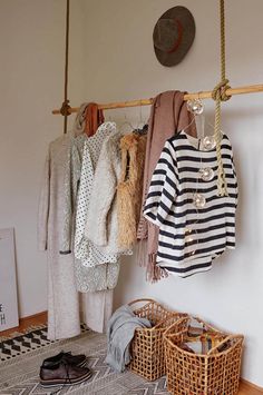 clothes are hanging on a rack in a room with baskets and rugs underneath it