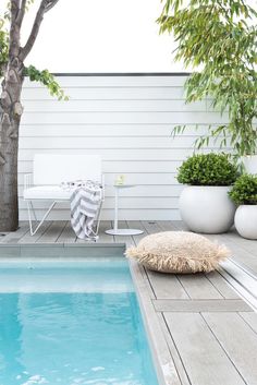 a small pool in the middle of a decked area with chairs and potted trees