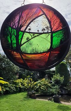 a circular stained glass window hanging from a pole in a garden with green grass and trees