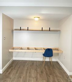 an empty room with a blue chair and some shelves on the wall, in front of a wooden floor