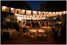 a group of people standing around tables with lights strung over them and hanging from the ceiling