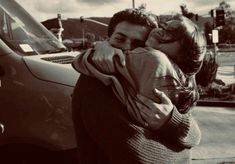 a man and woman hugging each other in front of a car on the side of the road