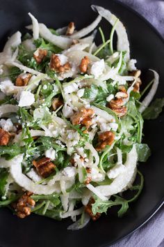 a black plate filled with salad and nuts on top of a white table cloth next to a fork