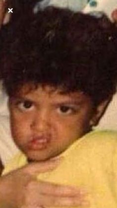 an old photo of a young boy with his hair pulled back and wearing a yellow shirt