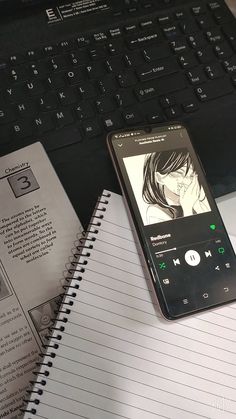 a cell phone sitting on top of a notebook next to an open book and keyboard