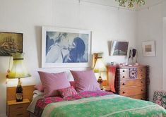 a bed with pink and green pillows in a bedroom next to a painting on the wall