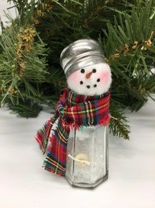 a small snowman in a plaid scarf and hat sitting inside a glass jar on top of a table