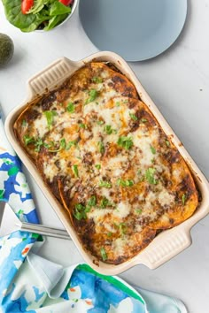 a casserole dish with cheese and vegetables in it on a white table next to other dishes