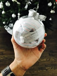 a hand holding a glass ornament in front of a christmas tree