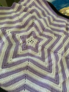 a purple and white crocheted blanket sitting on top of a bed next to a book