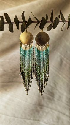 two pairs of earrings hanging from a branch with green beads and gold discs on it