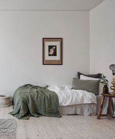 a bedroom with white walls and wooden flooring has a green blanket on the bed