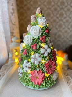 a small christmas tree made out of fake flowers on a white tablecloth with yellow lights in the background