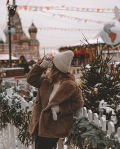 a woman standing in front of a christmas tree wearing a brown coat and white hat