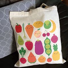 a white bag with fruit and vegetables on it sitting on a couch next to a pillow