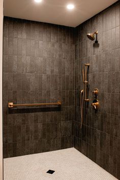 a walk in shower sitting next to a tiled wall with gold faucets on it