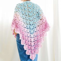 a woman wearing a pink and blue crocheted ponchy shawl, back view