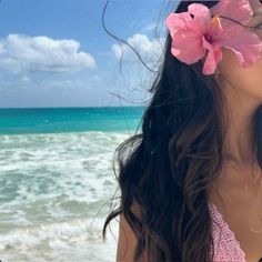 a woman with flowers in her hair standing on the beach looking at the water and sky