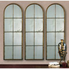 three arched windows with gold trim on each side and two vases next to them