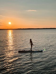 a person standing on a paddle board in the water at sunset or dawn, paddling