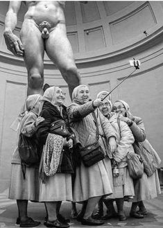 a group of people standing in front of a large naked man on top of a statue