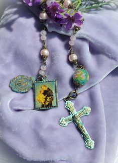 a cross and some beads are laying on a purple cloth with flowers in the background