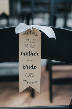 a mother of the bride sign hanging from a chair with a white ribbon on it