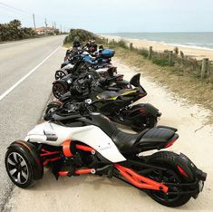 several motorcycles are lined up on the side of the road by the beach as people look at them