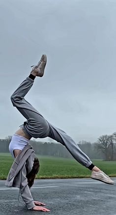 a woman is doing a handstand in the middle of an asphalt road with grass and trees behind her