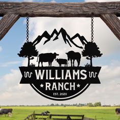 a sign hanging from the side of a wooden fence in front of cows and mountains