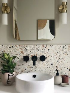 a white sink sitting under a bathroom mirror next to a potted plant on top of a counter