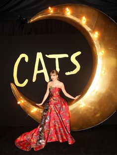 a woman in a red dress standing next to a gold moon with cats on it