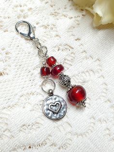 a pair of red beaded charms on a white lace surface with flowers in the background