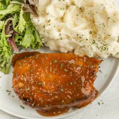 a white plate topped with meat covered in gravy next to mashed potatoes