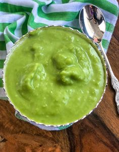 a bowl filled with green sauce on top of a wooden table next to a spoon