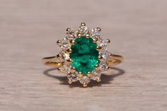 an emerald and diamond ring sitting on top of a wooden table