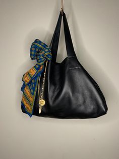 This slouchy black leather tote is hand stitched and made from locally sourced full grain leather. It features an interior pocket and an antuiqe brass lobster claw closure. The body measures a generous 16 1/2"w x 10"h x 5 1/2"d.  It's a great carry with a just a few items inside but can accommodate quite a bit as shown in the photos.  Try styling it by adding a short necklace or two as "bag charms" and layer in a silk scarf tied around the strap if you want a trendy look. It's also a great unisex utility tote if that's more your vibe. Super versatile! Slouchy Leather Tote, Silk Scarf Tying, Slouchy Bag, Utility Tote, Bag Charms, Black Leather Tote, Short Necklace, Full Grain Leather, Hand Stitched