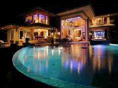 a large house that is lit up at night with lights on the pool and patio