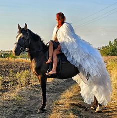 a woman in an angel costume rides a horse on a dirt road near a field