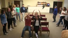 a group of people in a room with chairs and one person holding their hands up