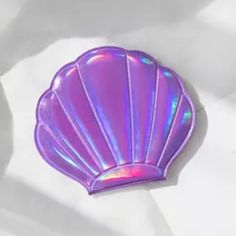 an iridescent shell shaped brooch sits on a white sheet, with shadows