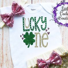 "This is an adorable St. Patrick's Day birthday outfit. This outfit features a bodysuit with the words \"Lucky One\". The outfit is complete with a matching gold headband and shorts. Other bottoms/headbands are available in my shop as well to choose from. HOW TO ORDER: 1.Bodysuit-Select Style and Size from the drop down and add to cart (S/S=Short Sleeve, L/S=Long Sleeve). 2.Add bottom and headband to complete the outfit for best value (optional). 3.Complete purchase and enjoy. All orders are cus Cute Birthday Bodysuit With Name Print, Cute Bodysuit With Name Print For Birthday, Customizable Cute Bodysuit For Birthday, Customizable Cute Birthday Bodysuit, Cute Customizable Onesie For Birthday, Customizable Cute Onesie For Birthday, Day Birthday Outfit, St Patrick's Day Birthday, St Patrick's Day Outfit