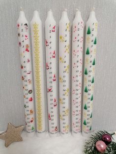 four white candles with christmas designs on them next to a small tree and star ornament