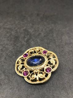 1928 Jewelry Company Victorian Brooch Blue Oval Faceted Glass Center, Purple Rhinestone Sets Filigree Style Quatrefoil Gold Finish Setting Victorian Revival Jewelry Set 1928 Jewelry Company Pressed Back Gold Tone Filigree Settings, Findings Vintage from 1970's-80's Size: 1 3/4 x 1 3/4 inches Condition: Very good; slight finish loss on pin back. Will be shipped First Class Mail in a gift box Blue Oval Brooch Jewelry, Oval Blue Brooch Jewelry, Oval Blue Brooch, Elegant Oval Blue Brooches, Elegant Blue Oval Brooches, Blue Oval Brooch, Vintage Sapphire Brooch Jewelry, Blue Oval Brooch For Formal Occasions, Elegant Blue Jeweled Brooches