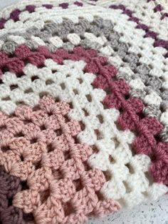 a crocheted blanket is laying on top of a white tablecloth with pink and gray squares