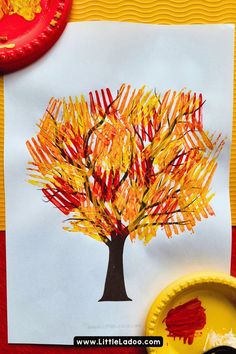 a paper plate with an autumn tree on it next to a red and yellow cupcake