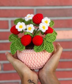 a small crocheted strawberry planter with daisies in it's center