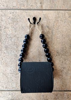 a black beaded purse hanging on a wall next to a tile floor with a hook