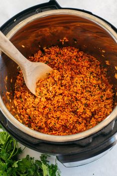 a wooden spoon in a pot filled with rice and parsley next to some cilantro