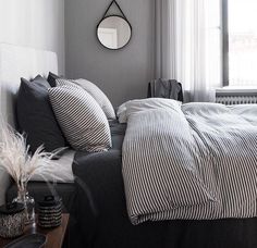 a bed with black and white striped sheets in front of a round mirror on the wall